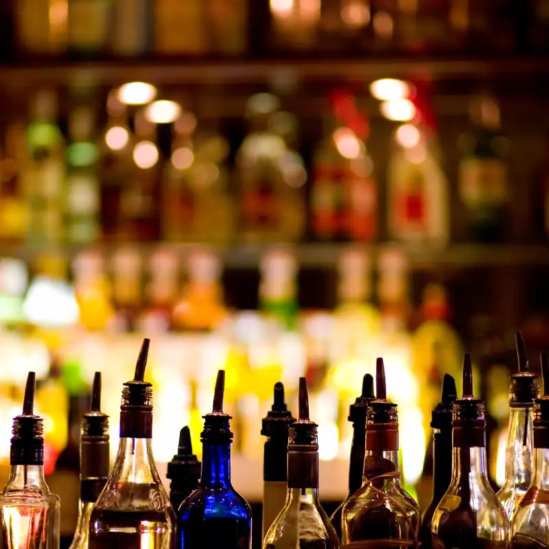 A bunch of bottles on top of a tabletop bar with pour spouts on them.